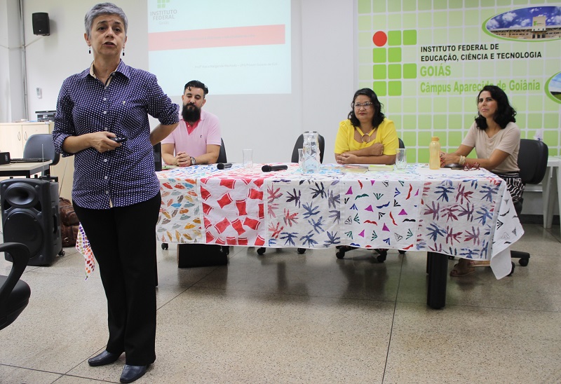 A palestra que tratou das especificidades da EJA nos institutos federais foi proferida pela professora Maria Margarida Machado (UFG), em pé, e pela professora Mad'Ana Ribeiro de Castro (IFG), ao centro da mesa com os coordenadores dos cursos técnicos em Alimentos e em Modelagem do Vestuário, respectivamente professores Sandro Henrique Ribeiro e Yane Ondina de Almeida A palestra que tratou das especificidades da EJA nos institutos federais foi proferida pela professora Maria Margarida Machado (UFG), em pé, e pela professora Mad'Ana Ribeiro de Castro (IFG), ao centro da mesa com os coordenadores dos cursos técnicos em Alimentos e em Modelagem do Vestuário, respectivamente professores Sandro Henrique Ribeiro e Yane Ondina de Almeida